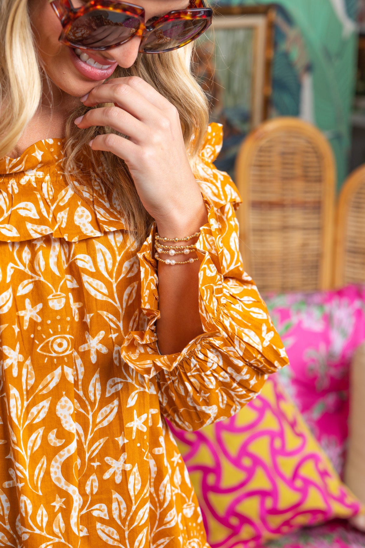 Woman wearing a yellow patterned dress with sunglasses and bracelets, sitting on a colorful couch.