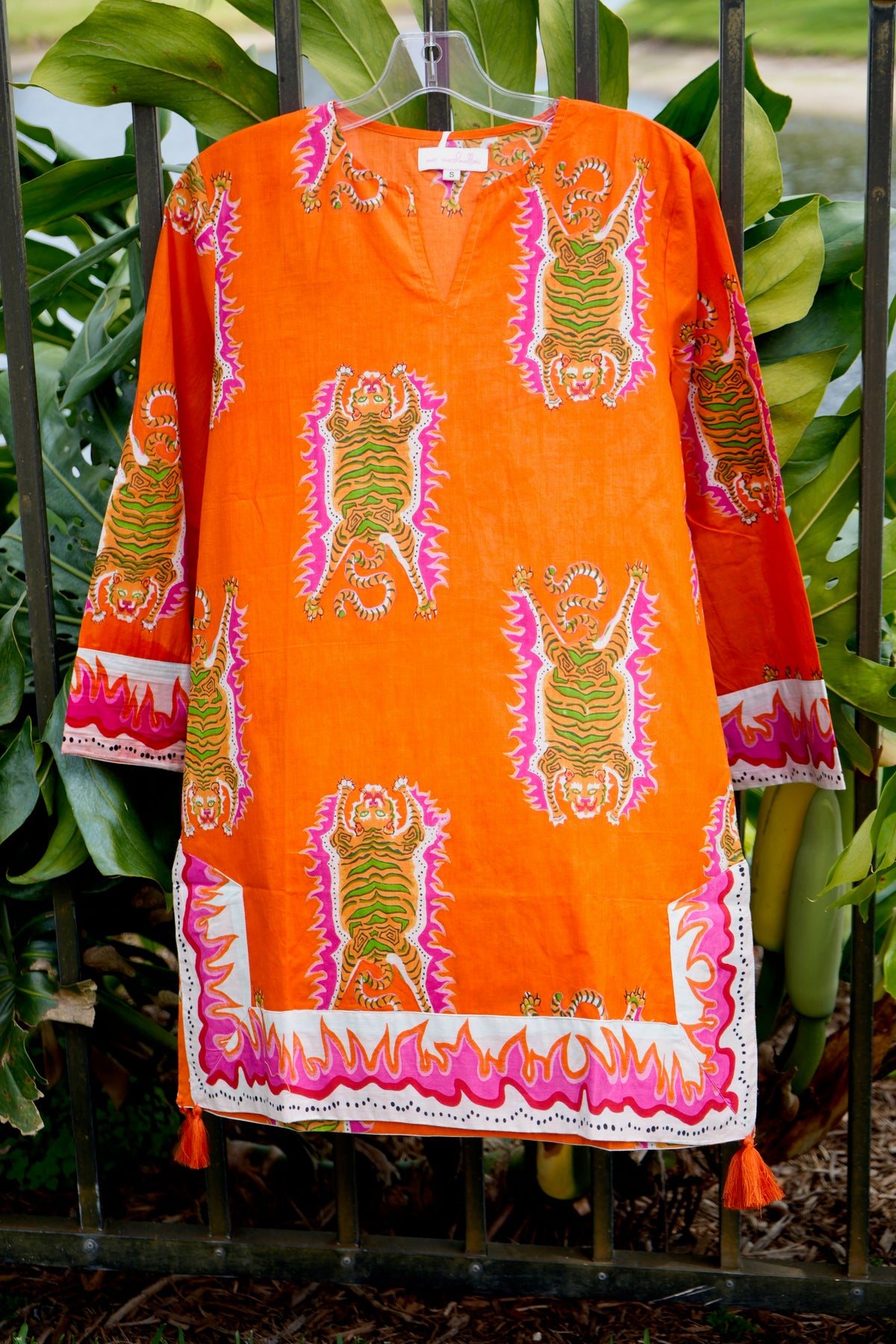 Orange dress with colorful patterns and tassels on a green leafy background