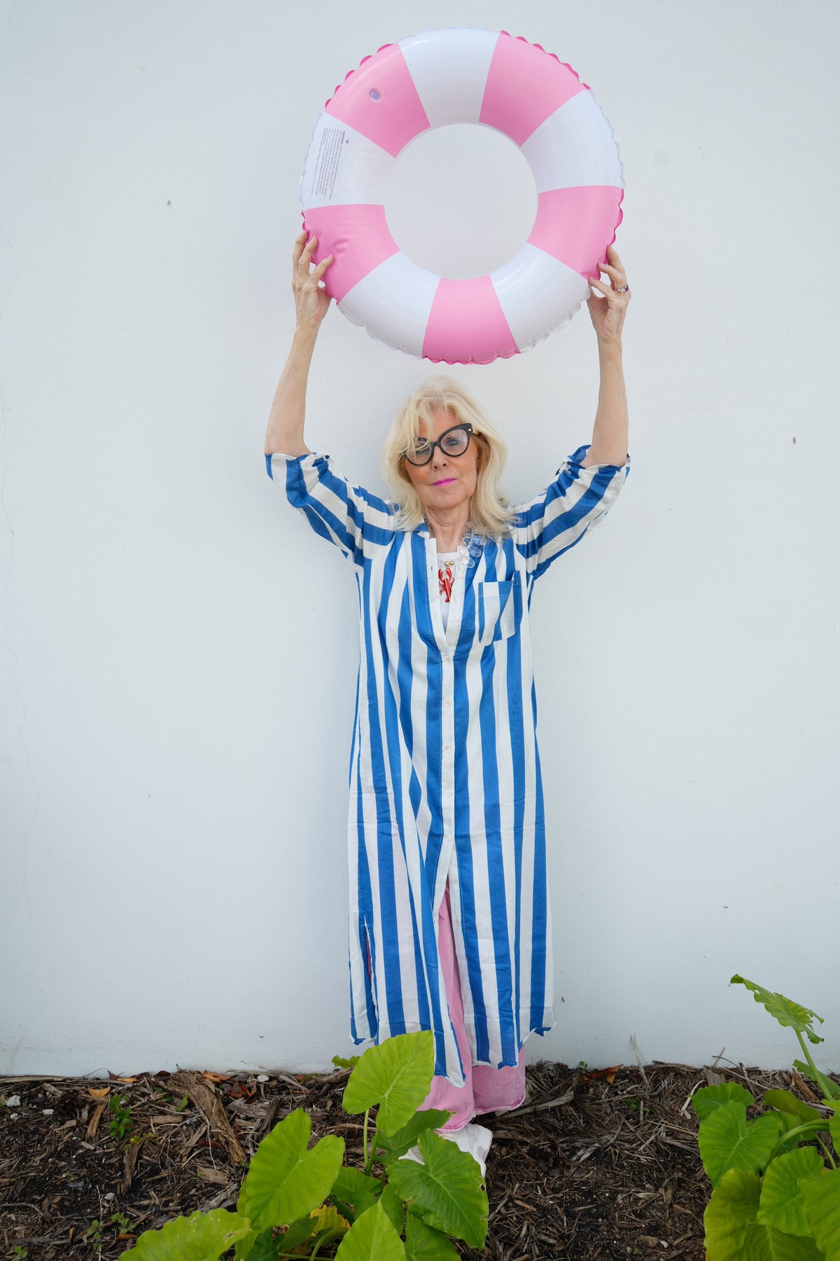 Person in a blue and white striped dress holding a pink and white life buoy against a white background.
